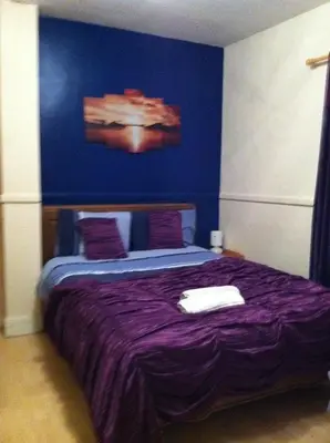 a bedroom with a purple bed with a blue wall at The Oasis Hotel in Harlow