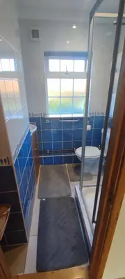 a blue tiled bathroom with a toilet and a window at Shear Annexe Flat in Cambridge