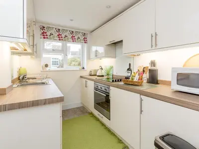 a kitchen with white cabinets and a green rug at Walnut Cottage in Aldeburgh