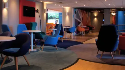 a waiting room with chairs and tables in a building at Holiday Inn Express London Stansted Airport by IHG in Stansted Mountfitchet