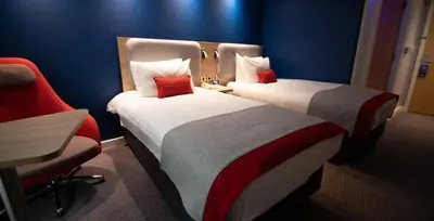 a hotel room with two beds and a red chair at Holiday Inn Express London Stansted Airport by IHG in Stansted Mountfitchet