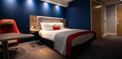 a hotel room with a bed and a red chair at Holiday Inn Express London Stansted Airport by IHG in Stansted Mountfitchet
