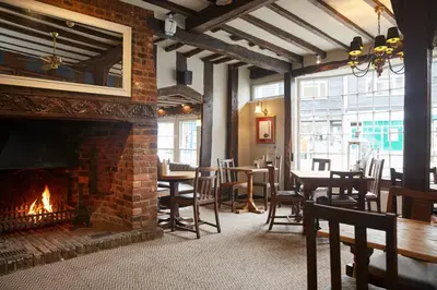 a restaurant with a brick fireplace and tables and chairs at White Hart Hotel by Greene King Inns in Coggeshall