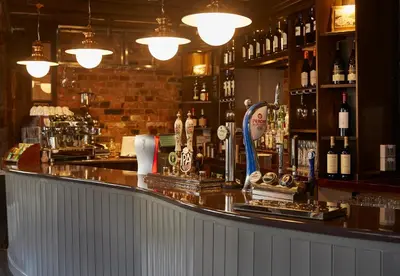 a bar with a counter with lots of bottles of alcohol at White Hart Hotel by Greene King Inns in Coggeshall