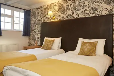 two beds in a hotel room with yellow and white at White Hart Hotel by Greene King Inns in Coggeshall