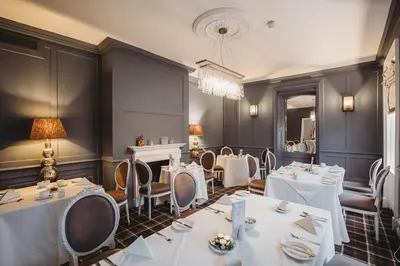 a restaurant with white tables and chairs and a chandelier at Greenwoods Hotel & Spa in Stock