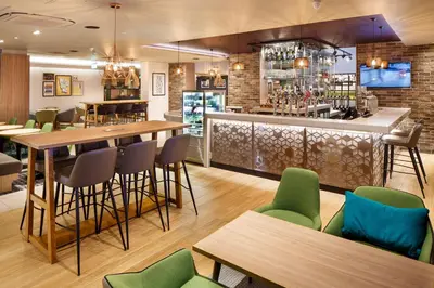 a restaurant with a bar with green chairs and tables at Holiday Inn Brentwood by IHG in Brentwood