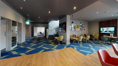 a waiting room with chairs and tables and a television at Holiday Inn Basildon by IHG in Basildon