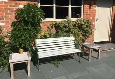 a white bench and two tables in front of a building at Snipe Vineyard Cottage in Woodbridge