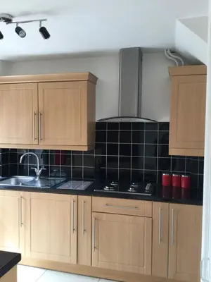 a kitchen with wooden cabinets and black tiles on the wall at 4 Bed House next to Basildon Town Centre in Basildon