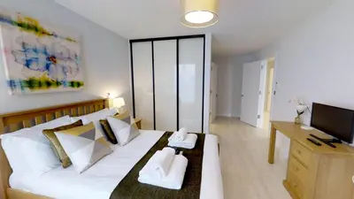 a bedroom with a white bed with a desk and a television at Signet Apartments - Vesta in Cambridge