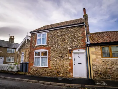 a brick house with a white door on a street at All Seasons Cottage Breaks in Saxmundham