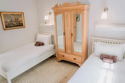 a bedroom with two beds and a wooden cabinet at Creeksea Place Barns in Burnham on Crouch