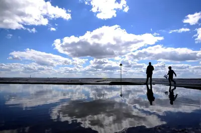 two people walking on the beach with a reflection in the water at Airport Reach in Southend-on-Sea