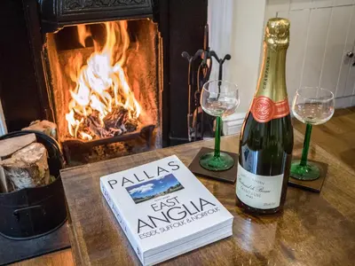 a bottle of wine and a book on a table with a fireplace at Pebble Cottage in Aldeburgh