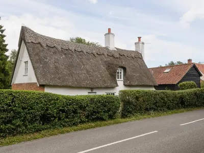 a white house with a thatched roof next to a road at Thatched Cottage in Saxmundham