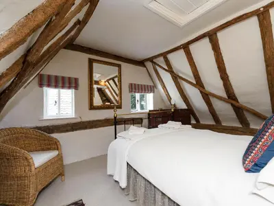 a bedroom with a white bed and a chair at Thatched Cottage in Saxmundham