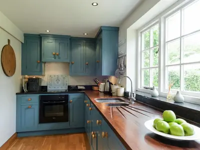 a kitchen with blue cabinets and a bowl of apples on the counter at Thatched Cottage in Saxmundham
