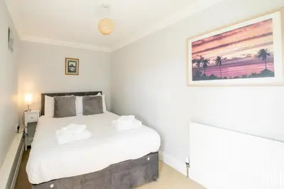 a bedroom with a white bed with a painting on the wall at 1 Hazelwood, Aldeburgh in Aldringham