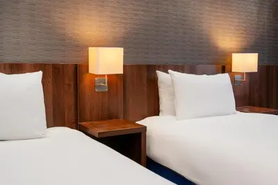two beds in a hotel room with two lamps at B&B Hotel Cambridge South in Cambridge