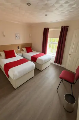 two beds in a bedroom with red curtains and a chair at The Railway Sleeper Lodge in Colchester
