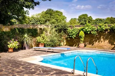 a swimming pool in a garden with a brick wall at Rectory Farm in Cambridge