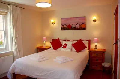 a bedroom with a white bed with red pillows at Seaside Fisherman Cottage Aldeburgh in Aldeburgh