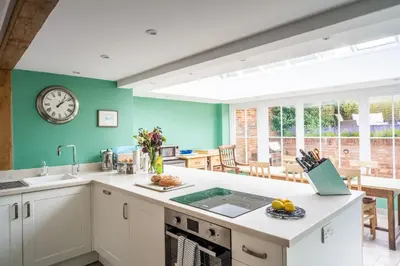 a kitchen with green walls and a clock on the wall at Myrtle Cottage in Friston