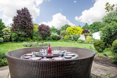 a table with plates and wine glasses in a garden at Vicarage House & Pool House in Hockham