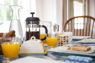 a breakfast table with orange juice and bread and a coffee maker at Vicarage House & Pool House in Hockham