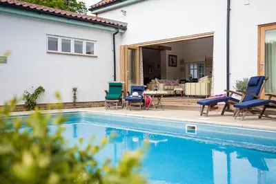 a pool with chairs and a table next to a house at Vicarage House & Pool House in Hockham