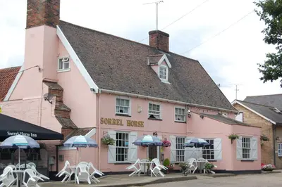 a pink building with white chairs and umbrellas at Sorrel Horse Inn in Ipswich