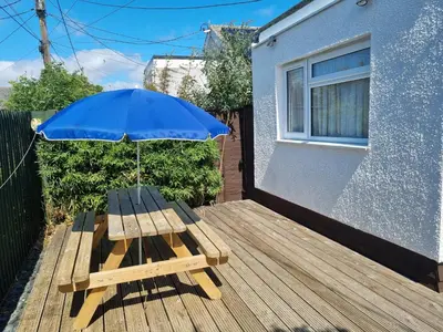 a wooden picnic table with an umbrella on a deck at Sandy Cottage in Clacton-on-Sea