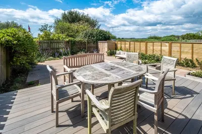 a patio with a wooden table and chairs on a deck at Lower Saltings in Aldeburgh