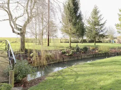 a pond in a park with trees and a fence at The Haybarn in West Bradenham