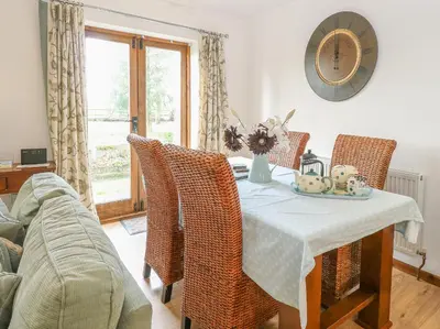 a dining room table with wicker chairs and a clock at The Haybarn in West Bradenham