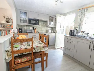 a kitchen with white cabinets and a table with a chair at Peggotty's in Kelsale