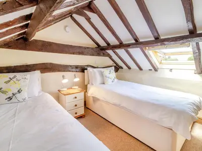 two beds in a room with wooden ceilings at Norbank Cottage in Bressingham