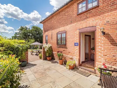 a brick building with a patio and a table at Punch Cottage in Little Glenham