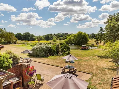 an outdoor patio with tables and umbrellas in a field at Punch Cottage in Little Glenham