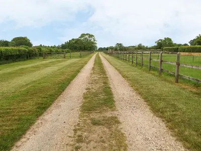a dirt road in a field next to a fence at Tawny Owl Barn in Shipdham