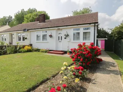 a white house with red flowers in the yard at Spurling Cottage in Cheveley
