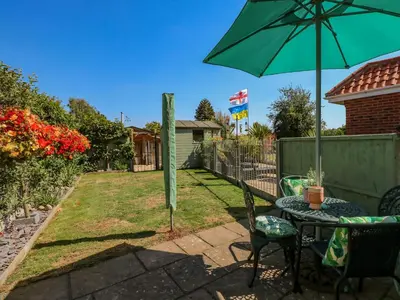 a patio with a table and a green umbrella at Cameron's Cottage in Swaffham