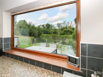 a large window in a bathroom with a view of a lake at Dragonfly Lodge in Yaxham