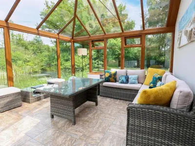 a conservatory with a glass table and chairs at Dragonfly Lodge in Yaxham