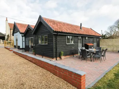 a small black cabin with a patio and a table at Whitehands Farm Barn in Old Buckenham