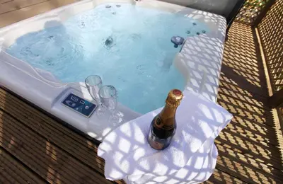 a hot tub with a bottle of champagne and glasses at Campion Lodge in Chappel