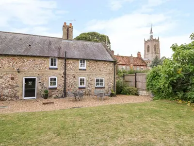 an old stone house with a courtyard and a church at Manor Farm Cottage in Swaffham