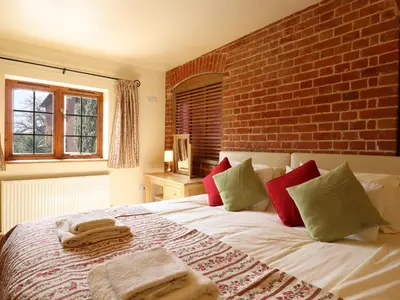 a bedroom with a bed with a brick wall at Poppy Cottage in Little Glenham