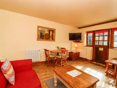 a living room with a red couch and a table at Poppy Cottage in Little Glenham